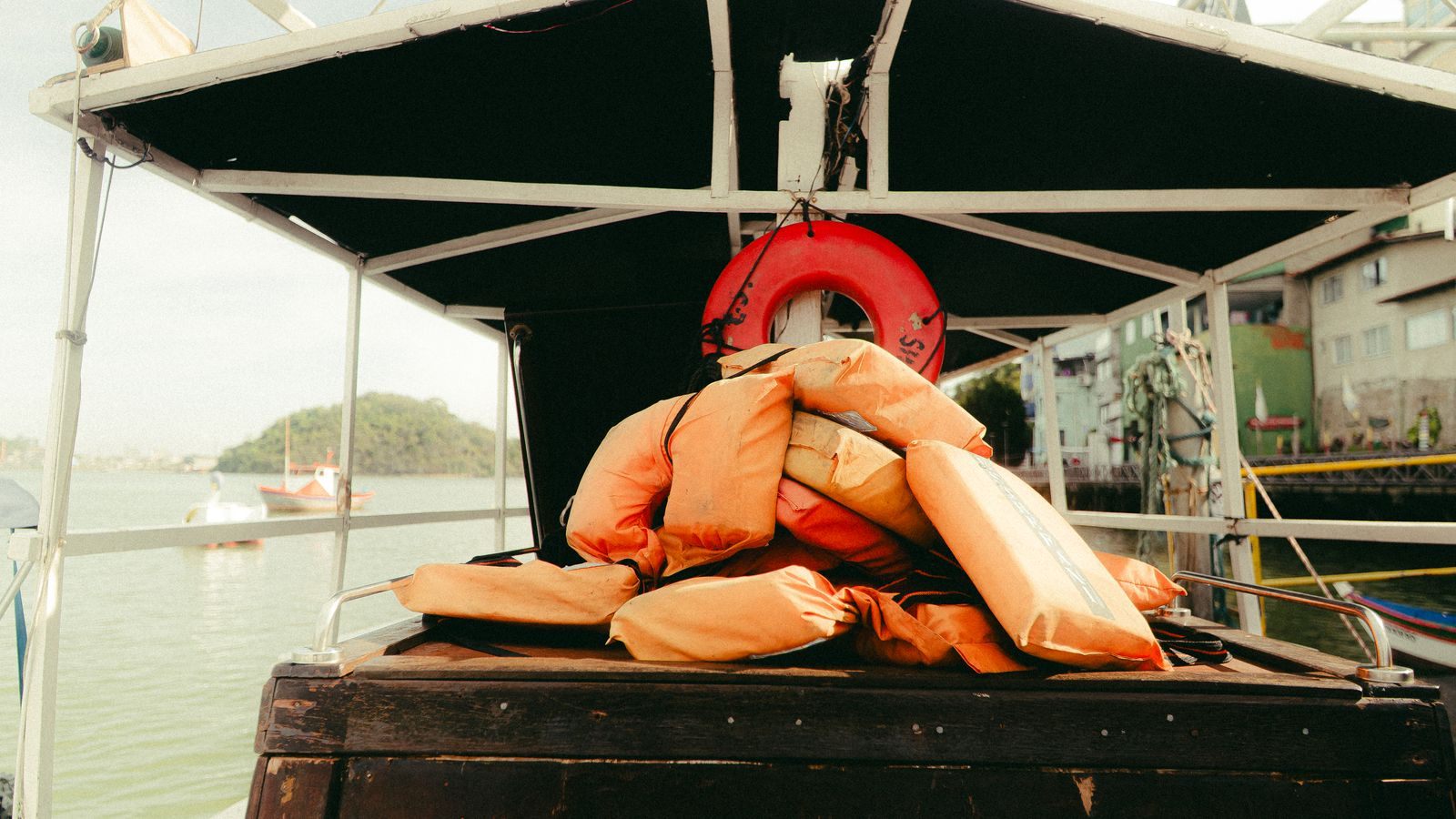 Orange life jackets and a life ring stowed under the canopy of a boat